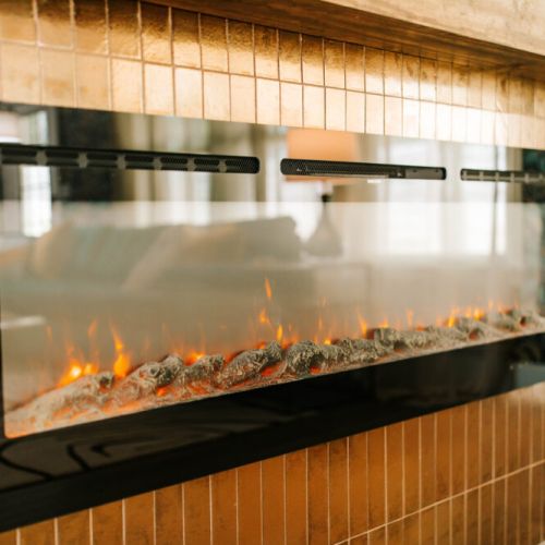 Cozy up next to this sleek, modern fireplace framed by shimmering gold tile—where luxe design meets ultimate relaxation. Perfect for unwinding with a glass of wine or starting your day with warmth and style.