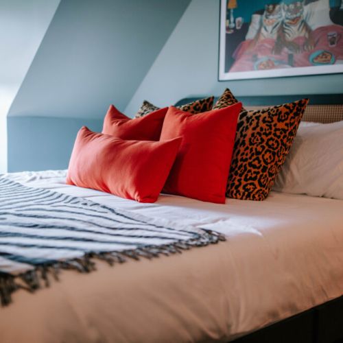 Sink into crisp linens and plush pillows after a day of exploring. Bold red and leopard-print accents add playful personality, while soft natural light and layered bedding create an inviting retreat made for slow mornings and restful nights.