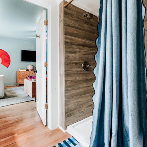 Refresh and recharge in this convenient bathroom featuring a walk-in shower with warm wood-look tile and a rainfall-style showerhead. With the living room just steps away, getting ready for the day or winding down at night feels effortless.
