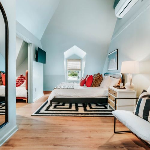 Retreat to this stylish bedroom with crisp linens, bold accent pillows, a wall-mounted TV, and charming architectural details. Unwind with your favorite show, settle into bed, and recharge in a space designed for restful nights.