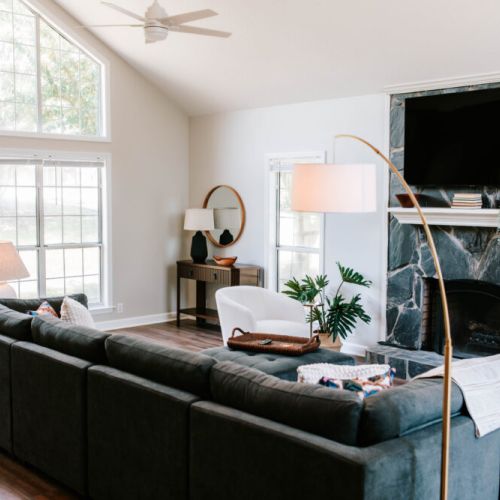 Sunlight pours into this stylish and comfy living room, featuring a cozy sectional, a statement stone fireplace, and a big-screen TV—perfect for movie nights, lounging, or just soaking in the chill vibes.