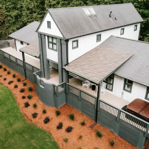 A stunning aerial view of the home, showcasing its wraparound porch, landscaped yard, and peaceful wooded surroundings.