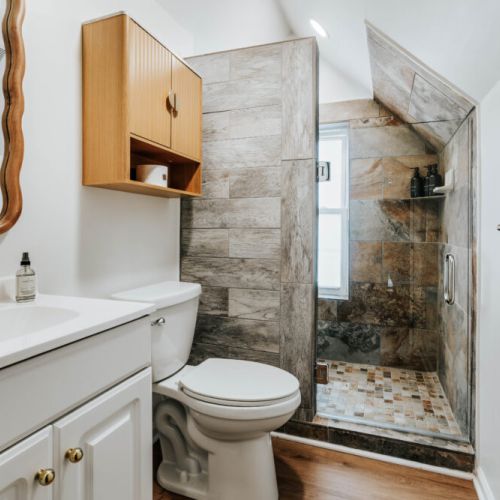 Refresh in this bright bathroom featuring a glass-enclosed walk-in shower with rich stone tile, provided bath essentials, and convenient vanity storage. A comfortable, thoughtfully designed space for getting ready or winding down.