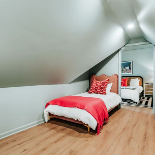 A charming bonus sleeping nook offers a private single bed with crisp linens and colorful accents. Tucked beneath the home’s unique sloped ceilings, it’s a welcoming spot for an extra guest to settle in and recharge.