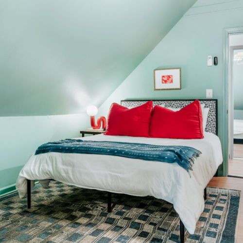 Recharge in this stylish bedroom with crisp linens, bold red accents, and distinctive sloped ceilings. A cozy, private retreat with thoughtful design details and a comfortable atmosphere for unwinding after a day of exploring.