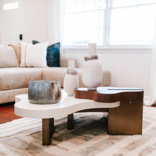 A bright, serene living space centered around an artful coffee table that blends organic shapes and soft, modern textures.