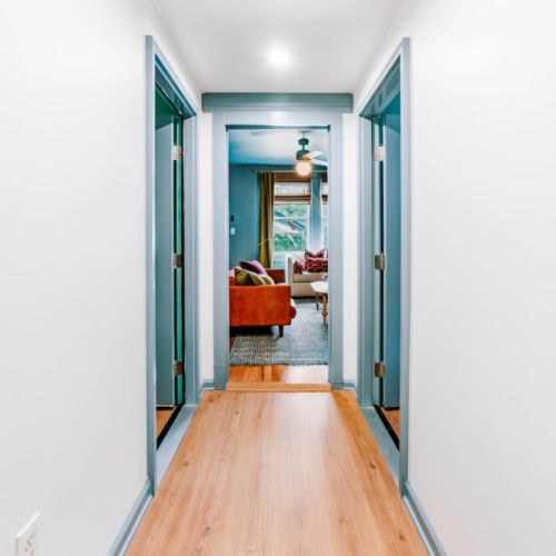 Move easily between bedrooms and shared spaces through this bright, welcoming hallway. Clean lines, warm wood floors, and colorful trim guide you toward the inviting living room, creating a comfortable flow throughout the home.