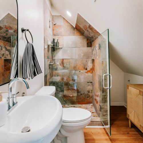 Refresh in this thoughtfully designed bathroom featuring a glass-enclosed walk-in shower with rich stone tile, provided bath essentials, and warm wood accents. A stylish, private space to start your morning or unwind before bed.