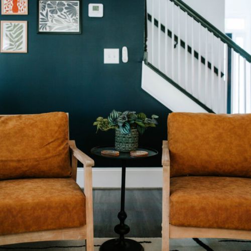 These cozy caramel armchairs are the perfect nook for your morning coffee or deep convos. Set against a moody navy wall and playful art—this is where vibes meet comfort.